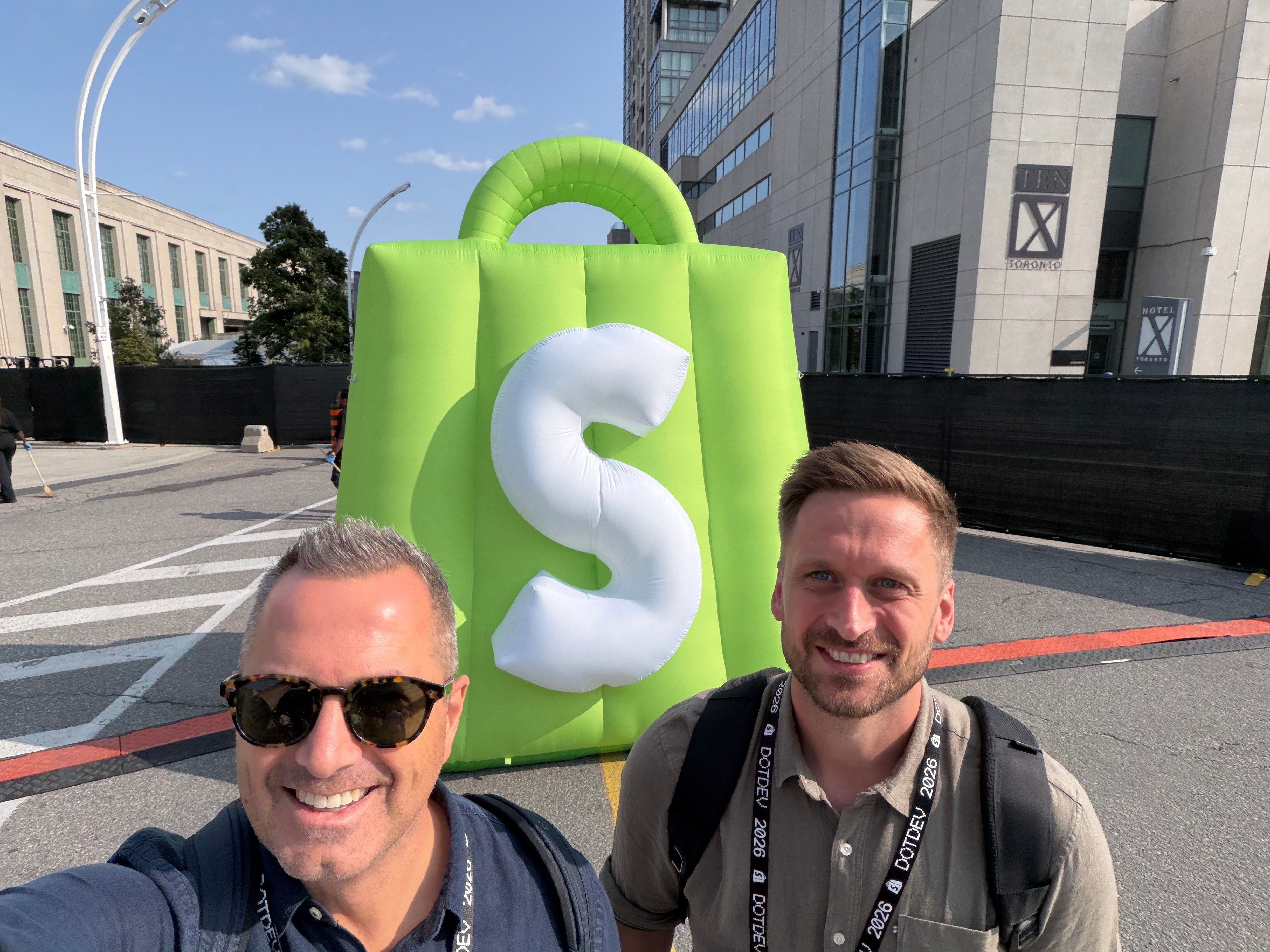 Alain Russell and James Lammas outside Shopify DotDev 2026 in Toronto, next to a giant inflatable Shopify bag